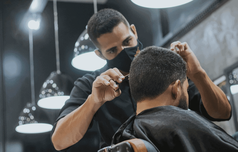 Barber wearing a black mask cutting a man's hair Barber wearing a black mask cutting a man's hair