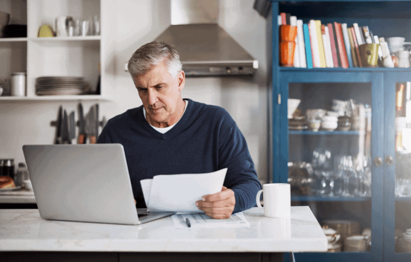 Man with grey hair wearing navy blue jumper and working on laptop Man with grey hair wearing navy blue jumper and working on laptop