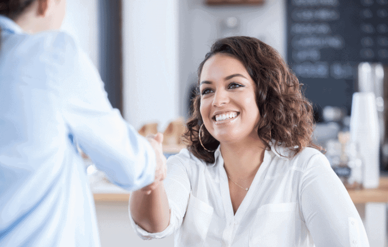 Woman wearing white shirt shaking hands with another woman Woman wearing white shirt shaking hands with another woman